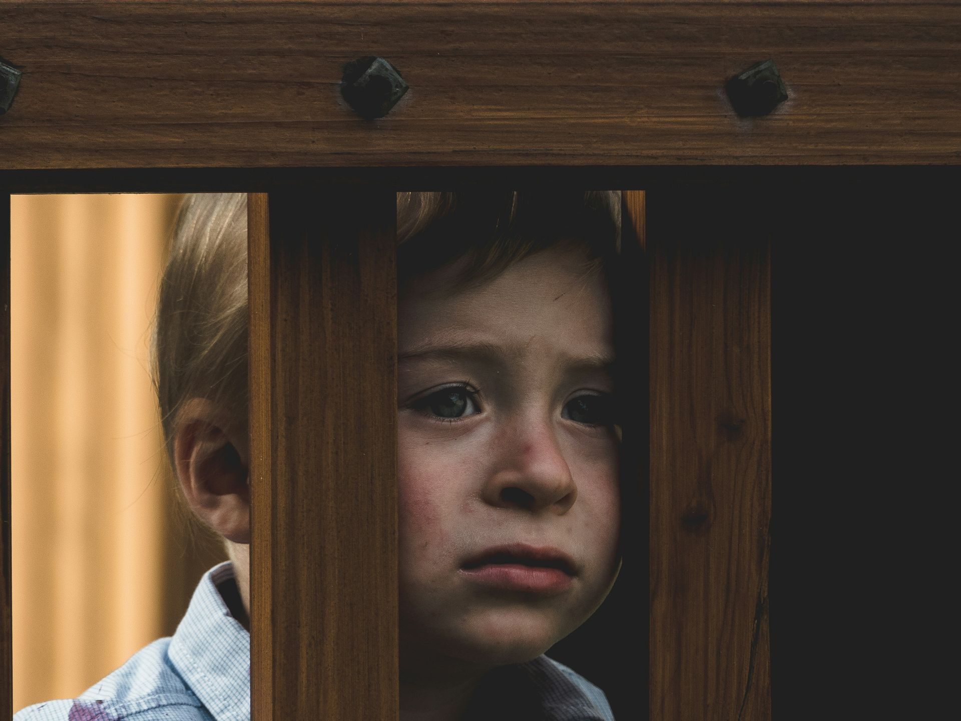 A young boy is looking through a wooden fence.