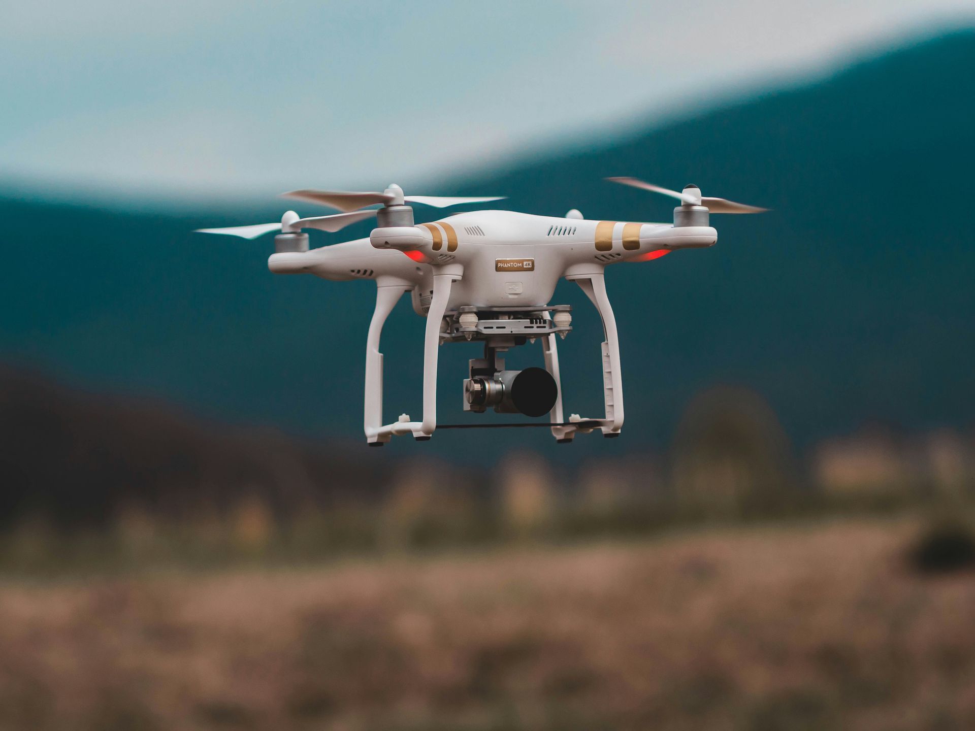 A drone is flying over a field with mountains in the background.