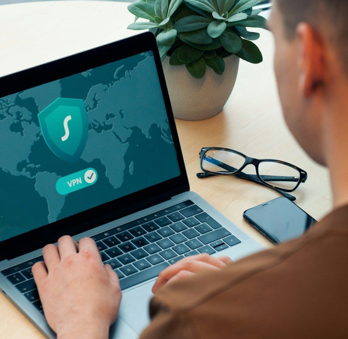 A man is typing on a laptop with a shield on the screen
