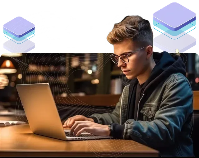 A young man is sitting at a table using a laptop computer.