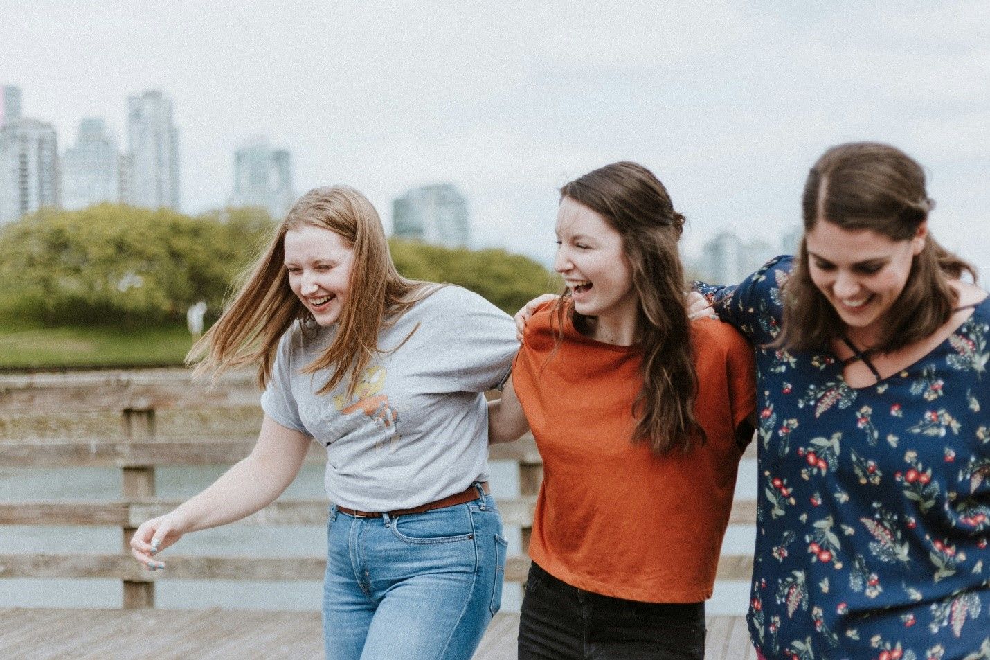 Three young women are walking on a wooden bridge and laughing.