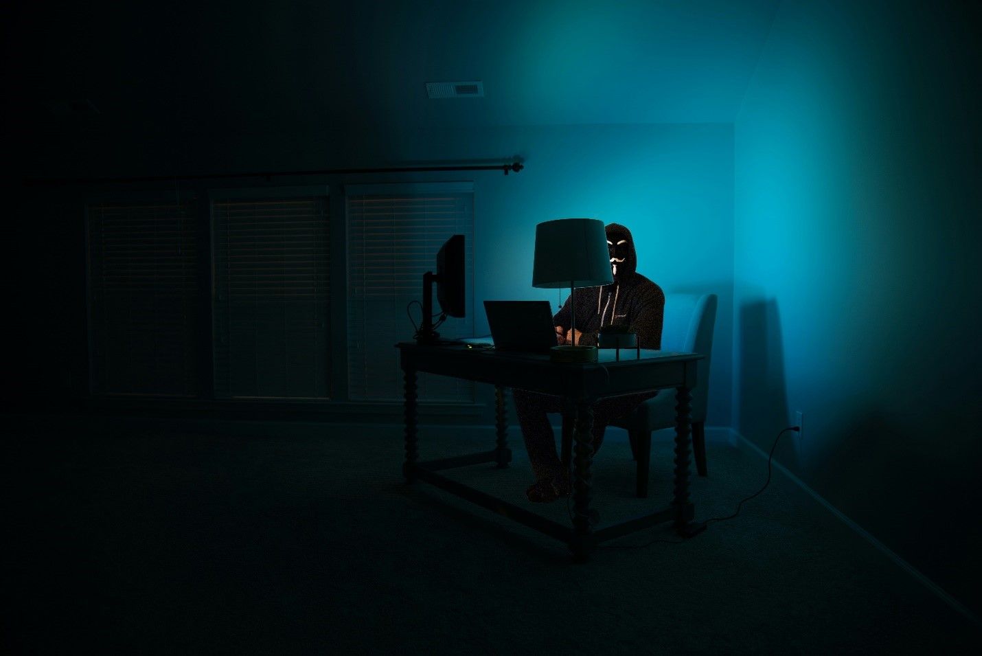 A man is sitting at a desk in a dark room using a laptop computer.