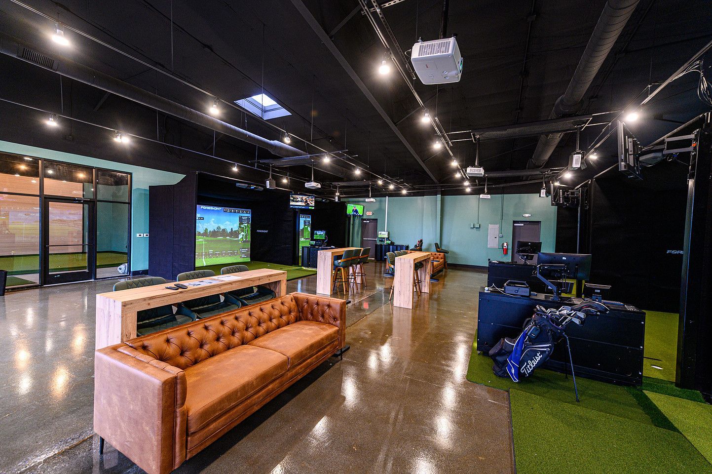 People playing cornhole on a rooftop patio with brick walls, green turf, and city views.