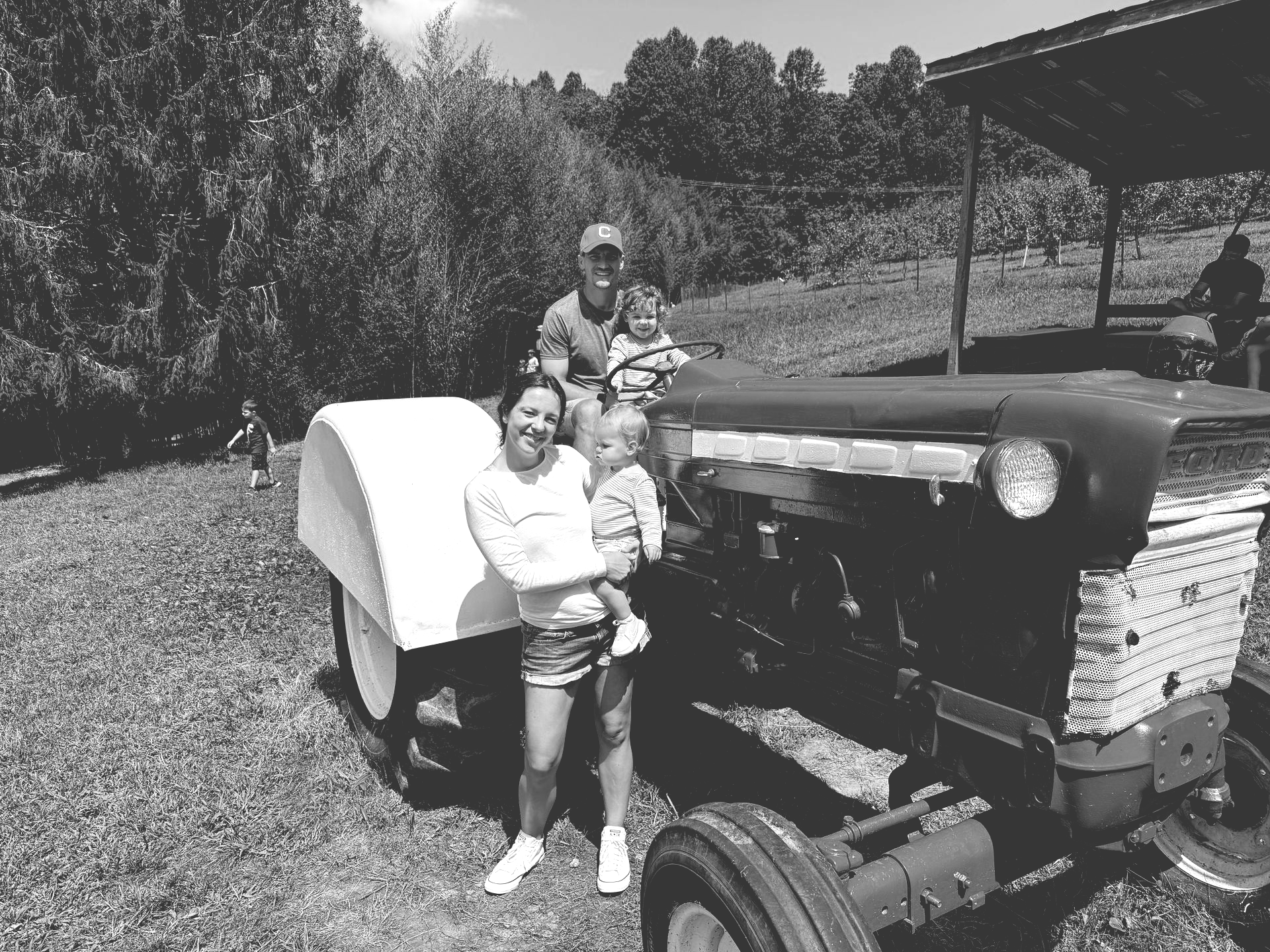 Family posing on a blue tractor in a grassy field on a sunny day.