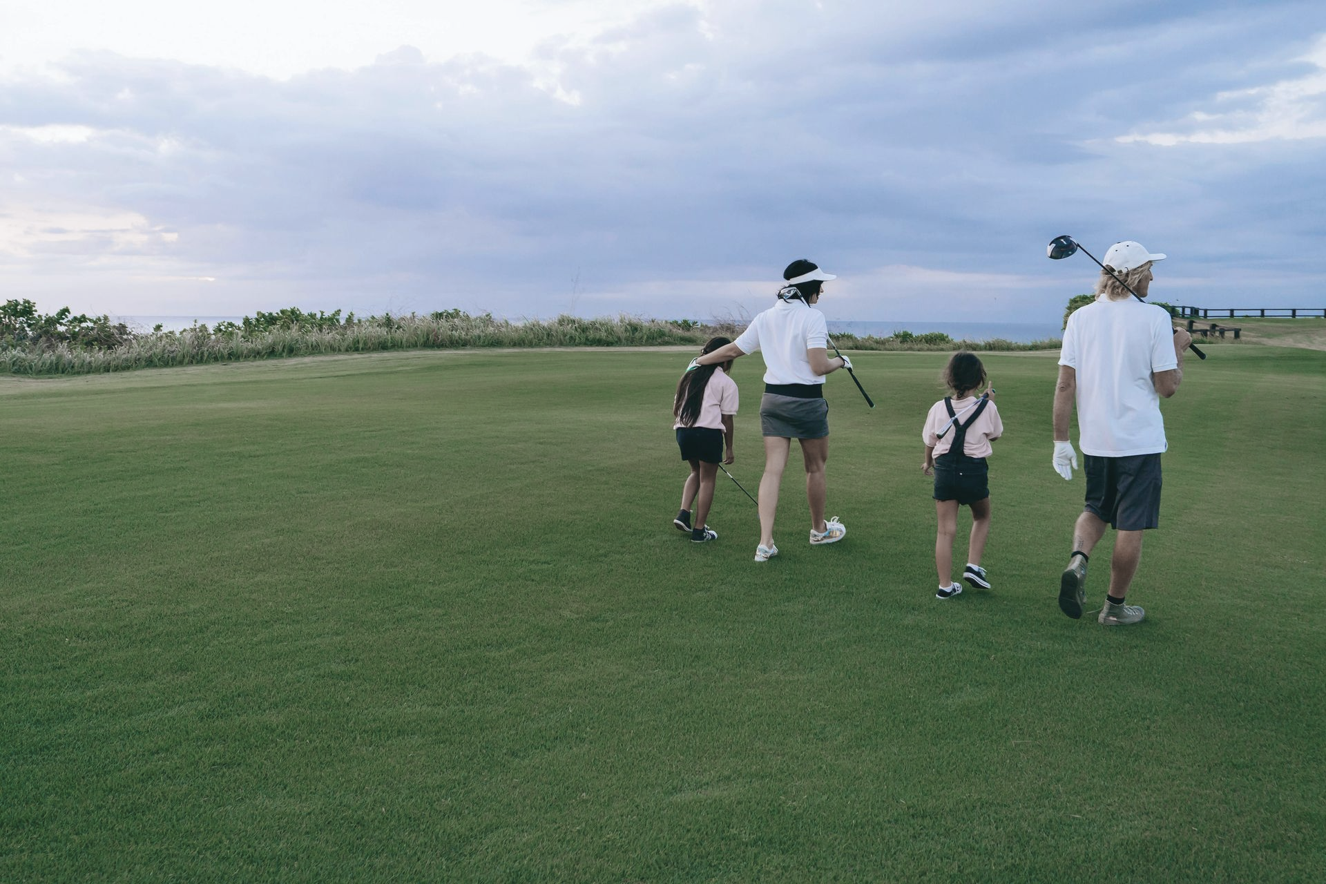 Two men on a golf course posing with golf clubs; one has a hat and shorts, the other has a cap and pants.