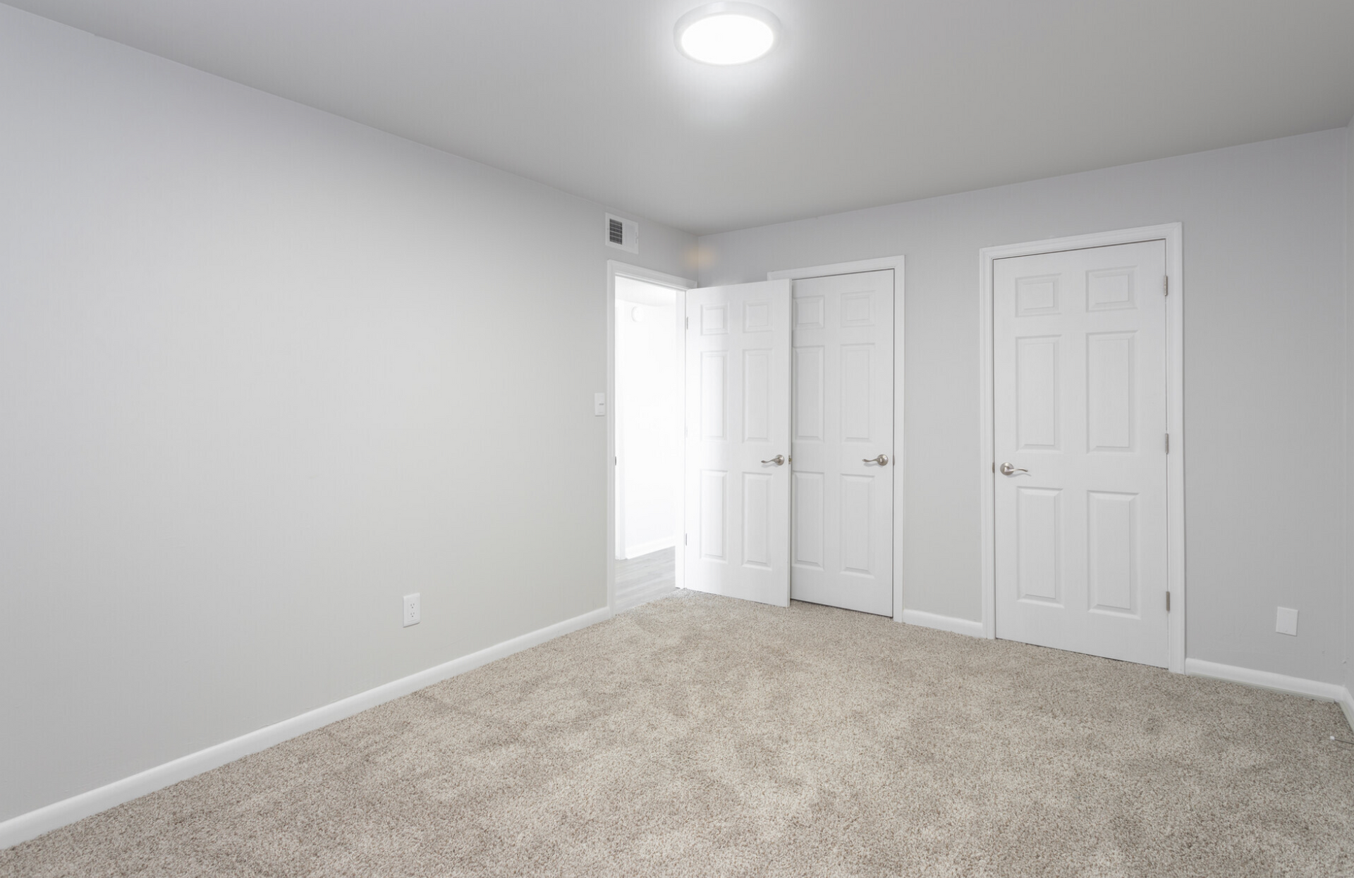 An empty bedroom with a carpeted floor and white walls.