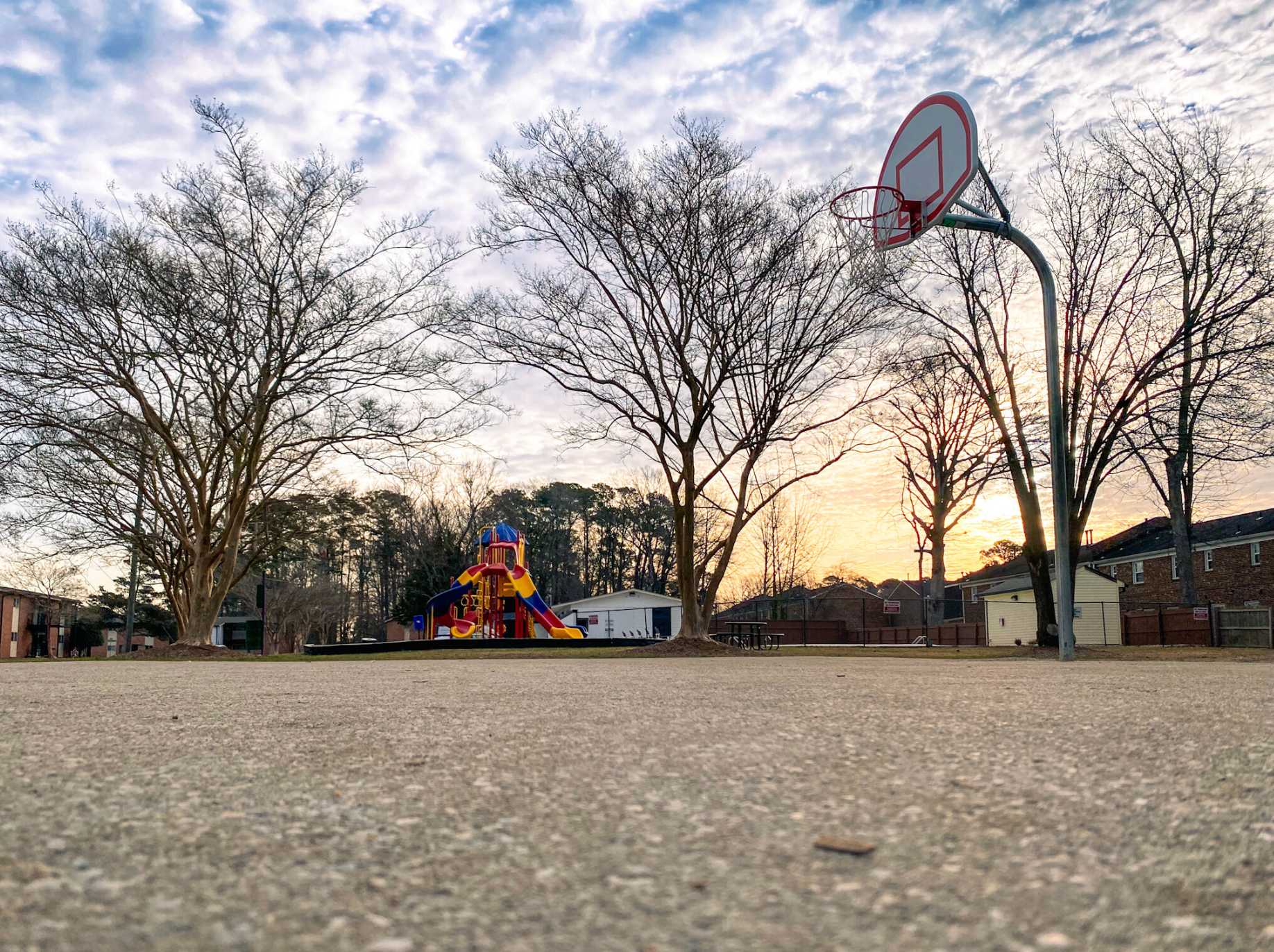 A basketball hoop in a park with a playground in the background.