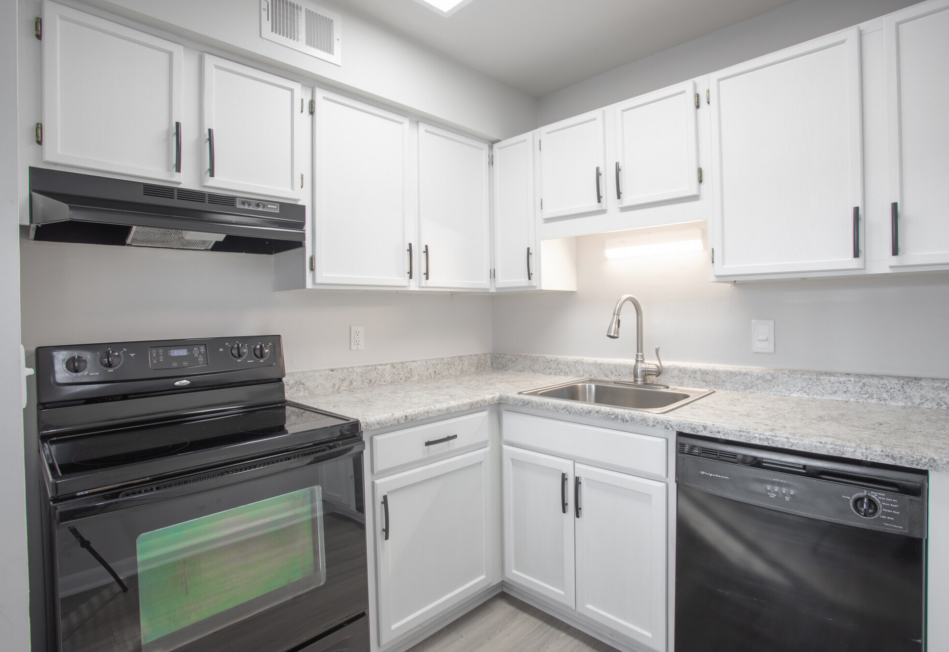 A kitchen with white cabinets , a stove , a sink , and a dishwasher.
