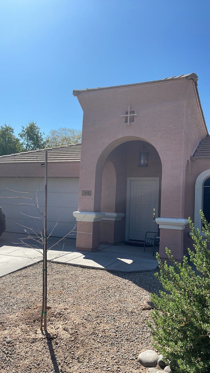 A house with a sprinkler in front of it and a tree in front of it.