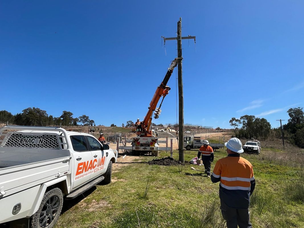 Workers using a crane to work on a utility pole with power lines on a sunny day.