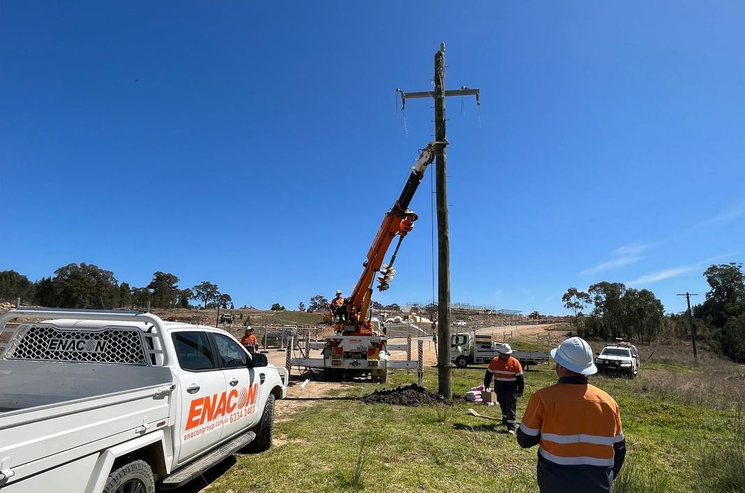 Workers using a crane to work on a utility pole with power lines on a sunny day.