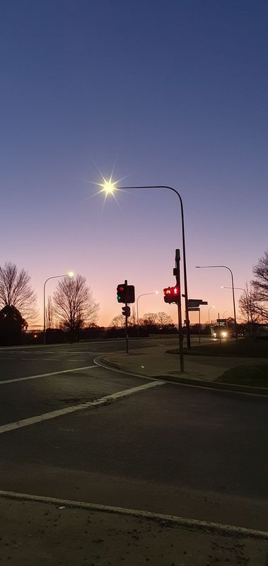 Dusk at a street intersection; a glowing street lamp illuminates the road. Red traffic light against a colorful sky.