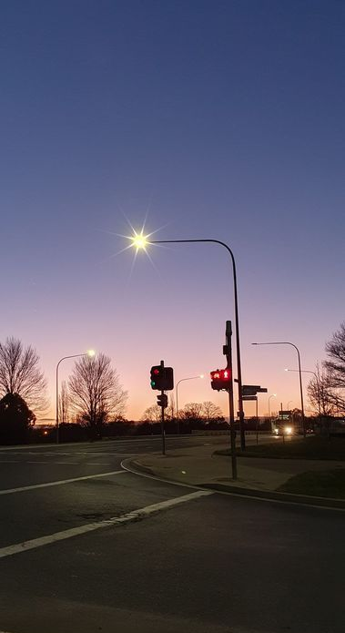 Dusk at a street intersection; a glowing street lamp illuminates the road. Red traffic light against a colorful sky.