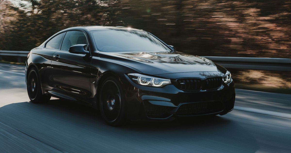 A black bmw m4 is driving down a road. | InTown Auto Care