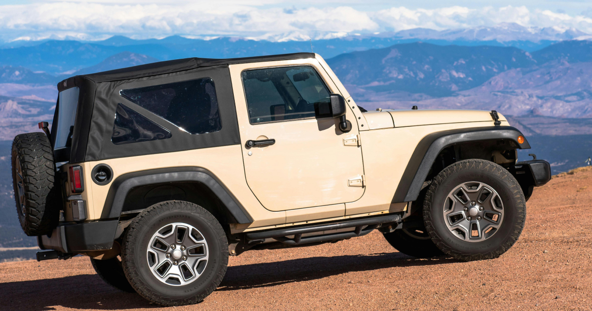 A jeep is parked on top of a dirt hill with mountains in the background. | InTown Auto Care