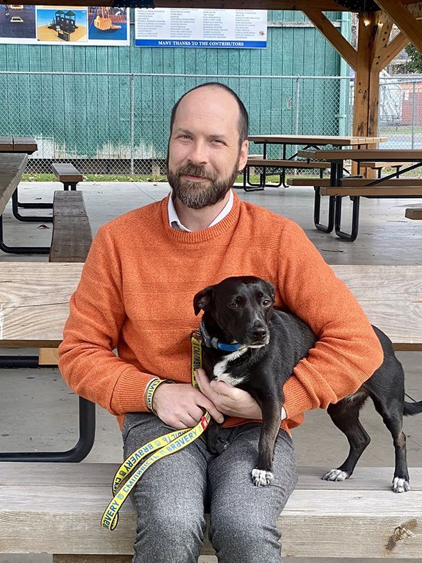 A man is sitting on a bench holding a black dog. | InTown Auto Care