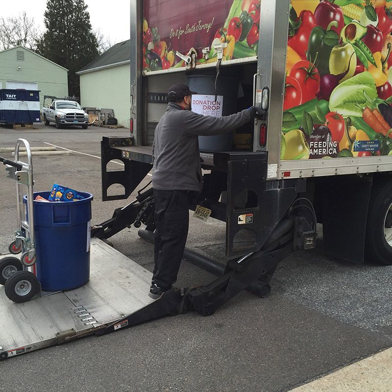 A man is loading a container into a truck that has a fruit and vegetable advertisement on it | Intown Auto Care