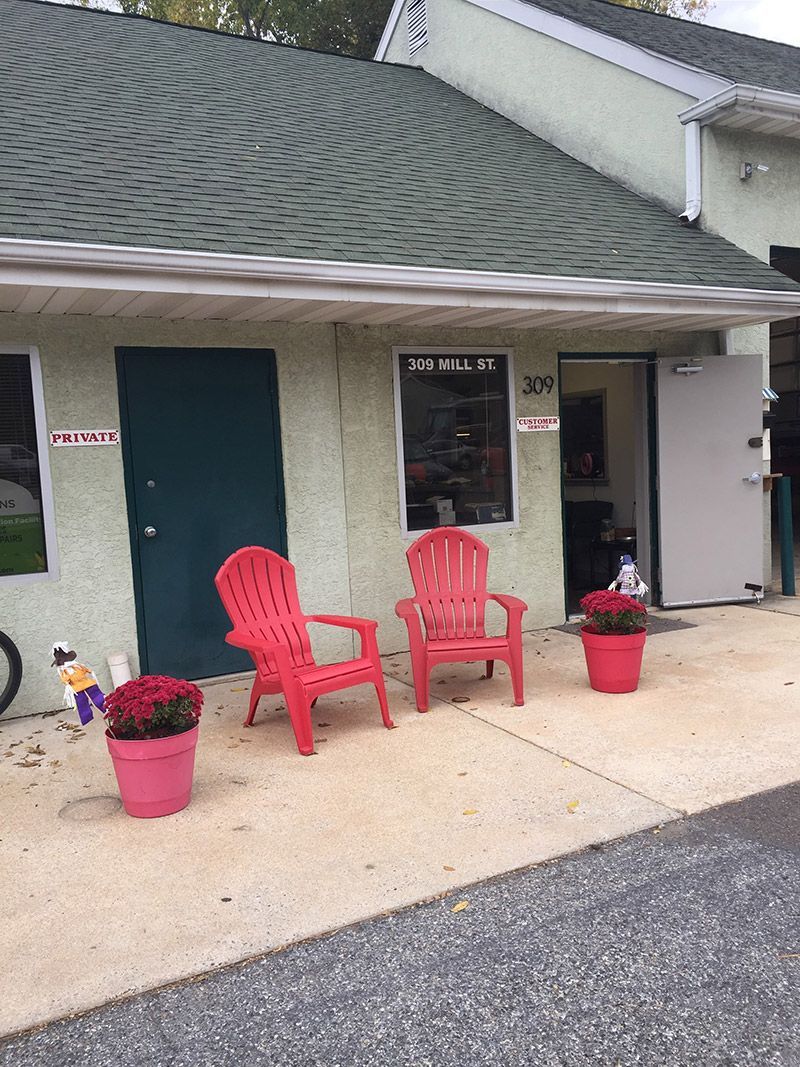 A house with red chairs and pink potted flowers in front of it. | InTown Auto Care