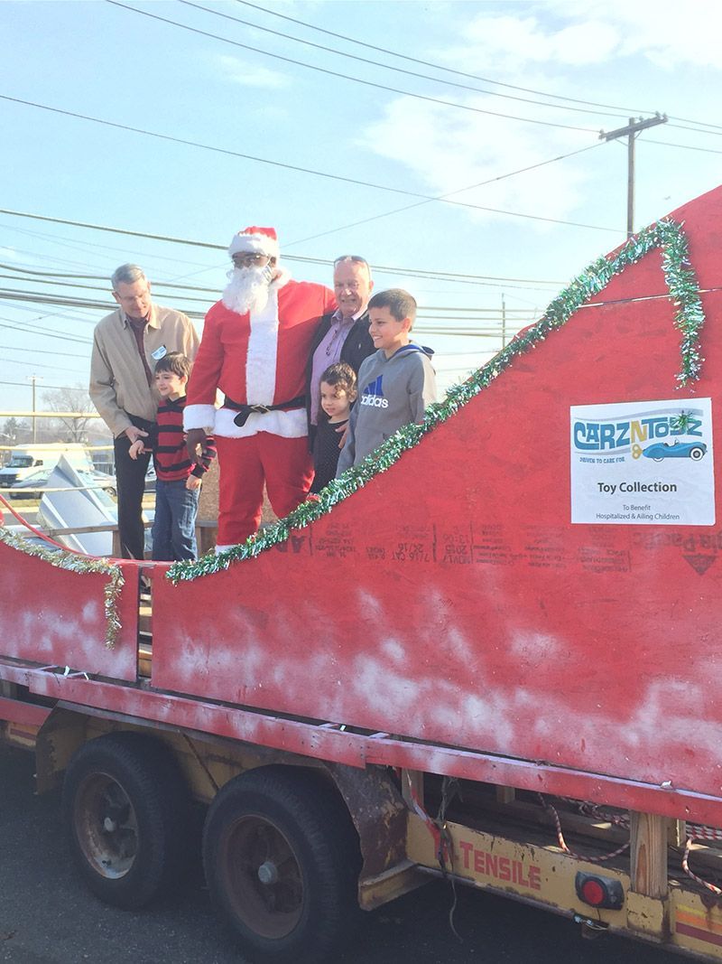 A group of people are standing on top of a red float with santa claus on it. | InTown Auto Care