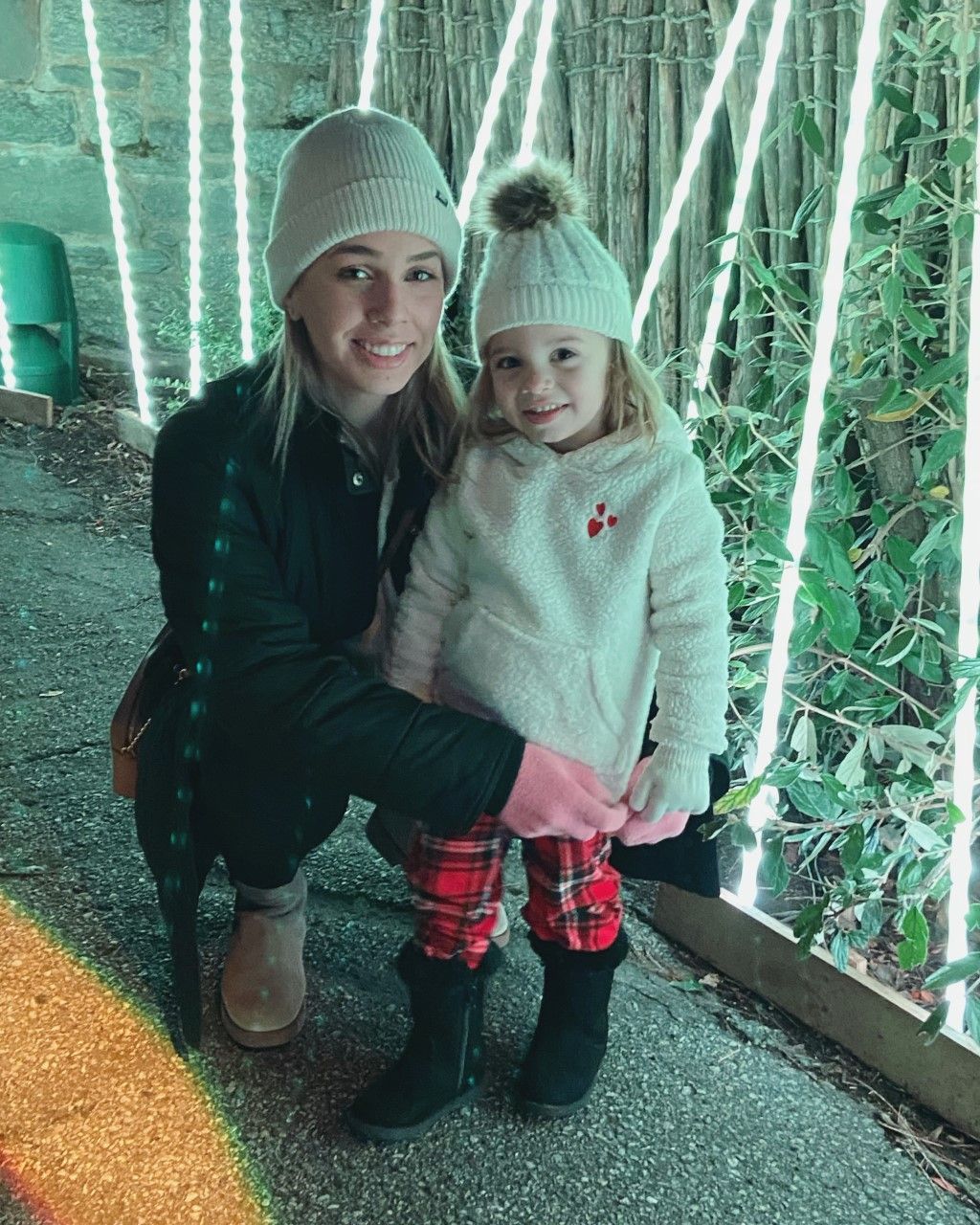 A woman is kneeling down next to a little girl wearing matching hats. | InTown Auto Care