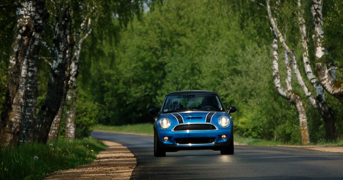 A blue mini cooper is driving down a country road. | InTown Auto Care