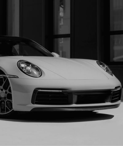 A white porsche 911 is parked in front of a building in a black and white photo. | InTown Auto Care