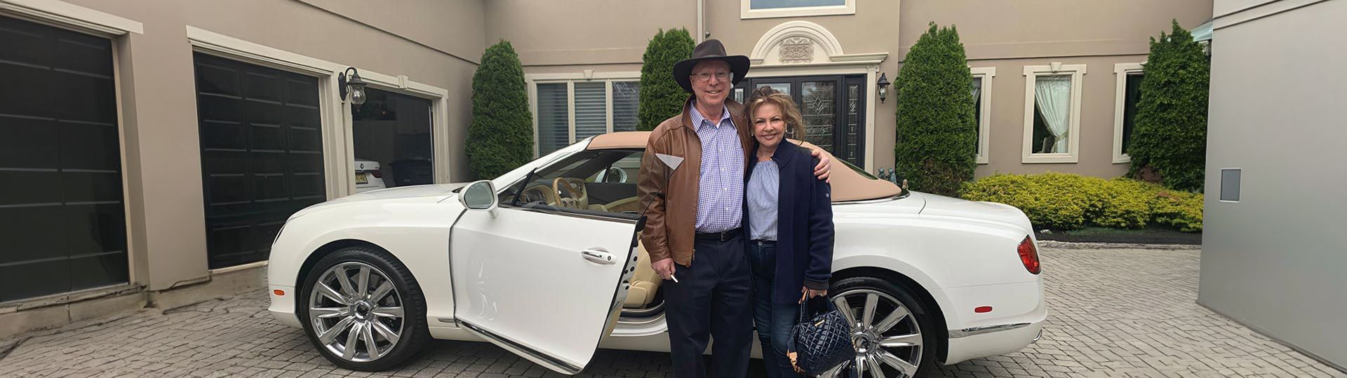 A man and woman are standing next to a white car in front of a house. | InTown Auto Care