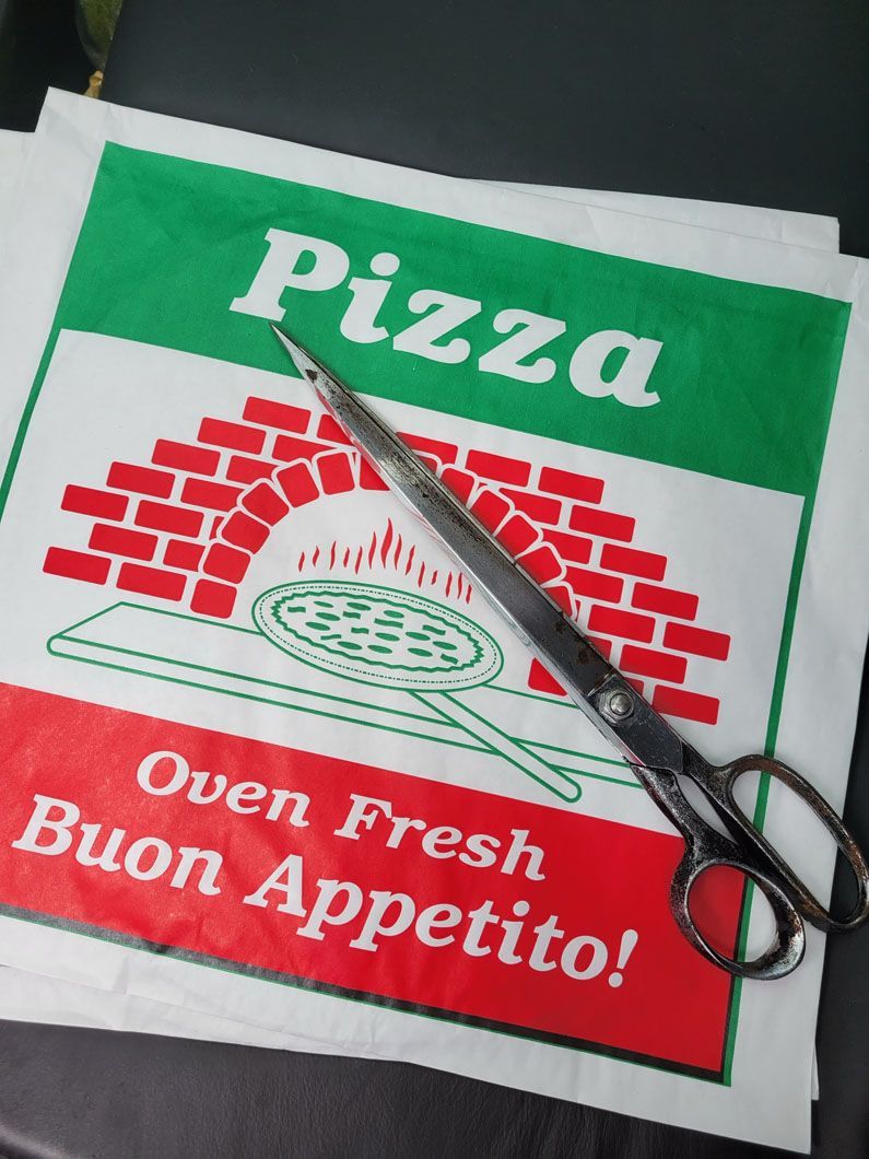 A pair of scissors sitting on top of a napkin that says pizza oven fresh buon appetito