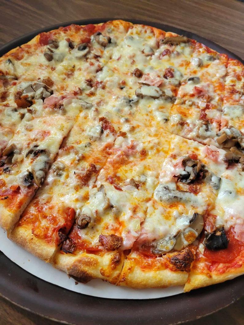 A pizza with a lot of toppings on it is on a pizza pan on a table.
