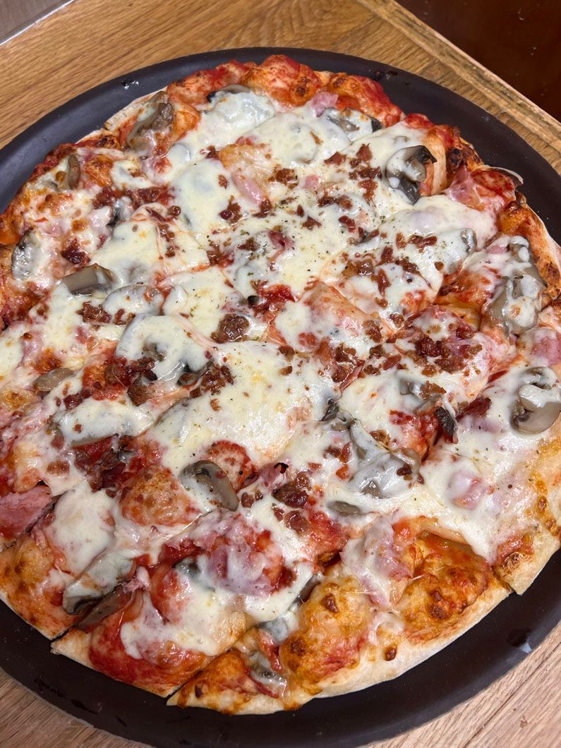 A pizza is sitting on a black pan on a wooden table.