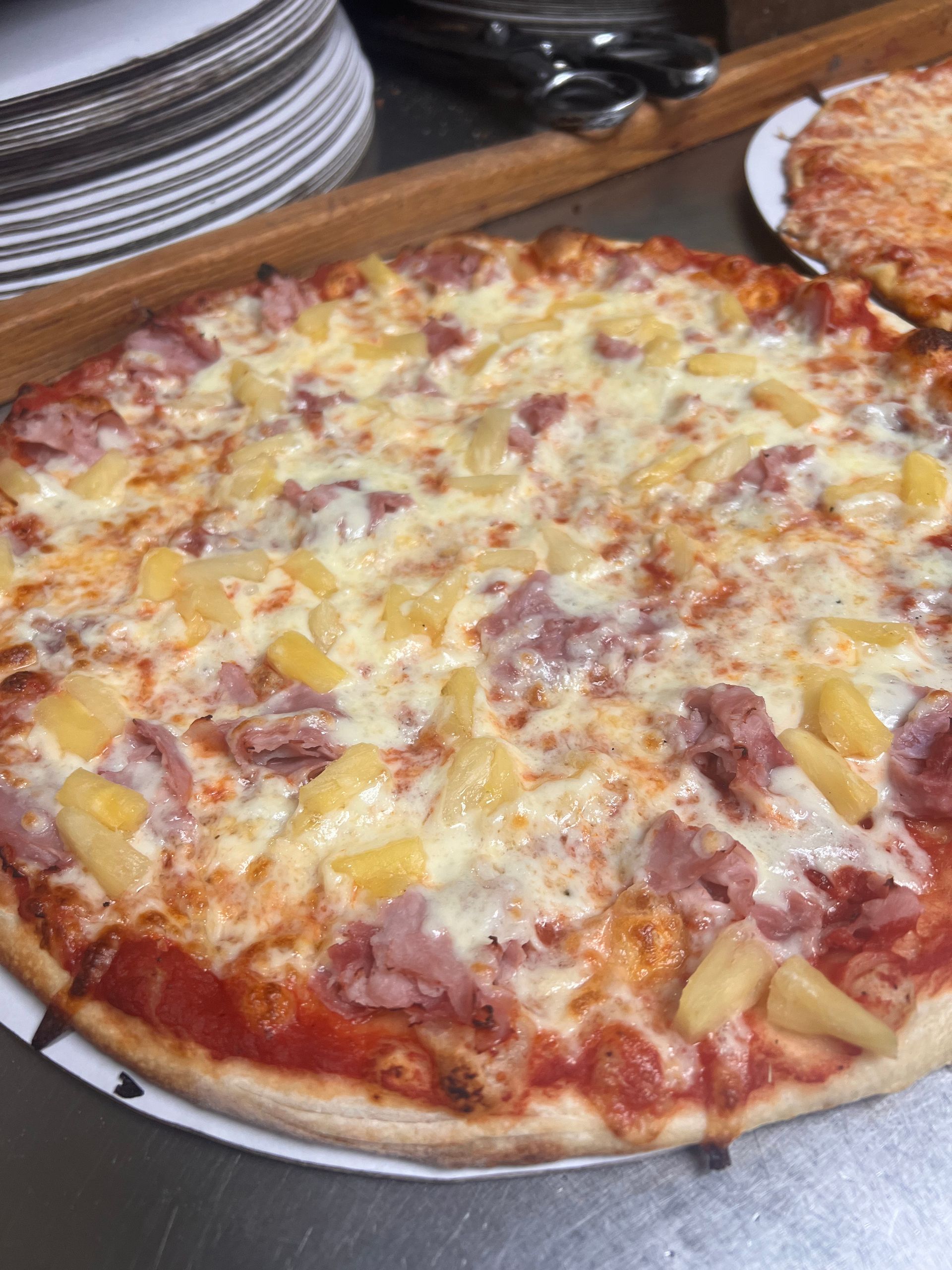 A pizza with pineapple and ham is sitting on a pan on a table.