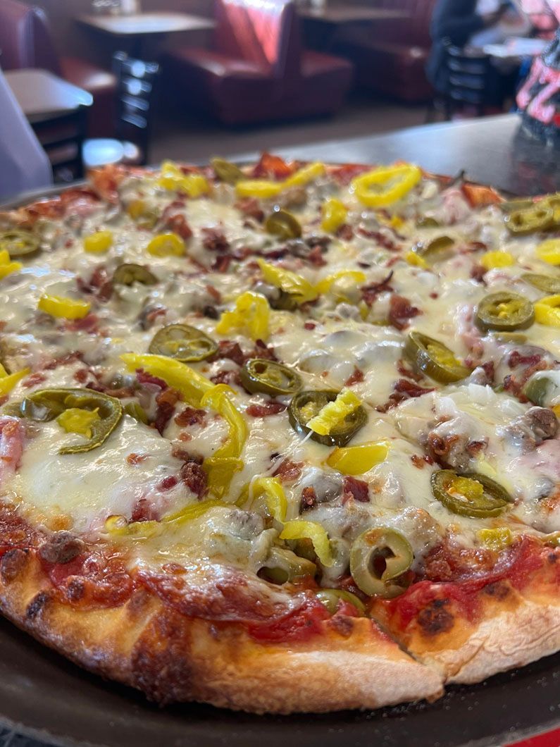A pizza with pepperoni , olives , jalapenos and cheese on a pan.