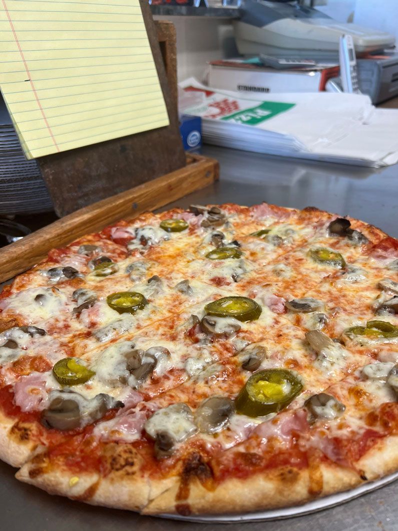 A pizza with jalapenos , mushrooms , and cheese is on a pan on a table.