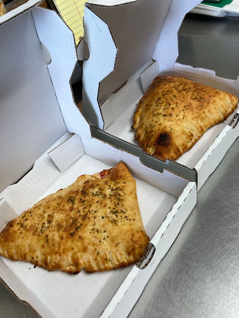 Two slices of pizza in white boxes on a counter
