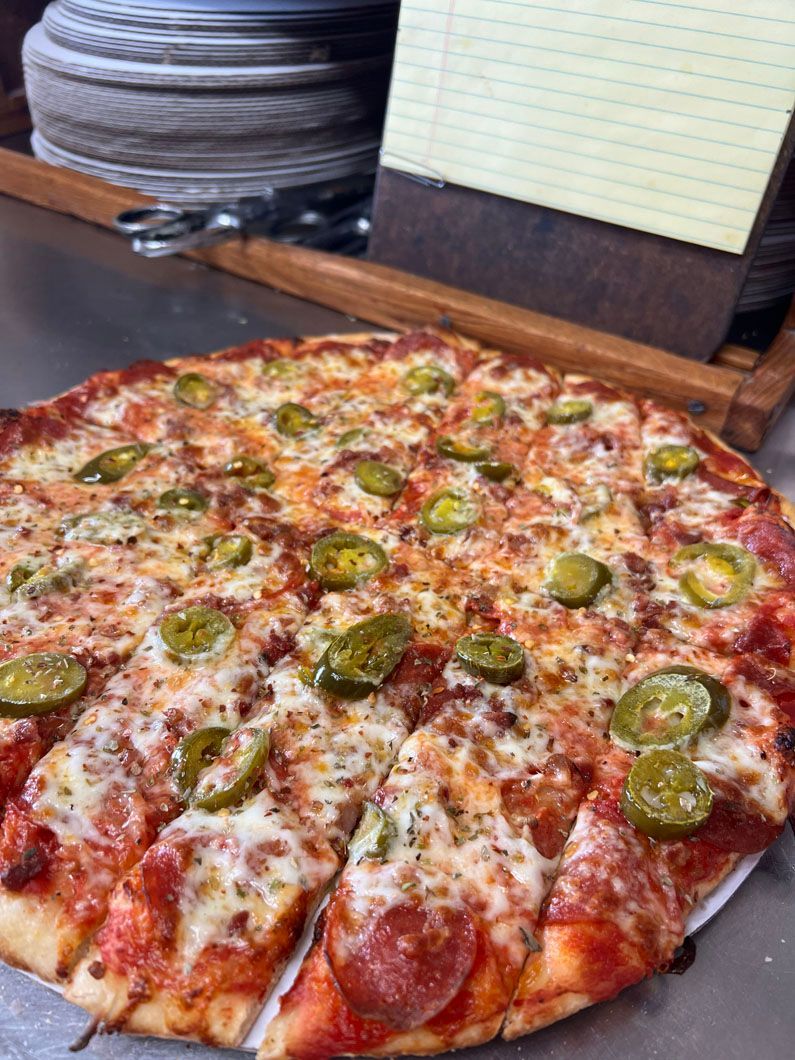 A pizza with pepperoni and jalapenos on it is sitting on a table.