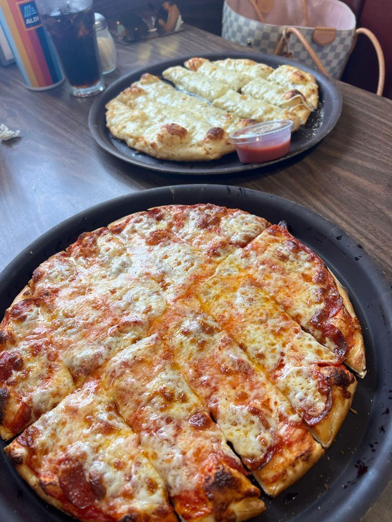 Two pizzas are sitting on a wooden table next to each other.