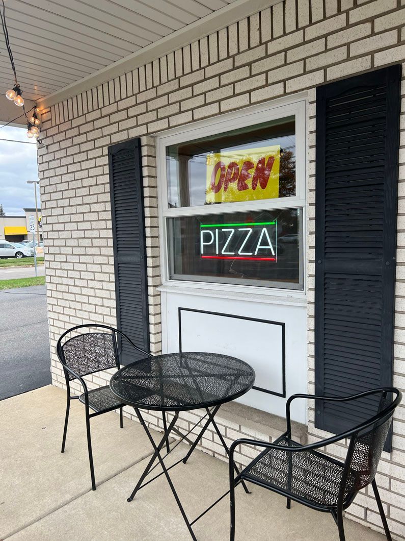 There is a table and chairs outside of a pizza restaurant.
