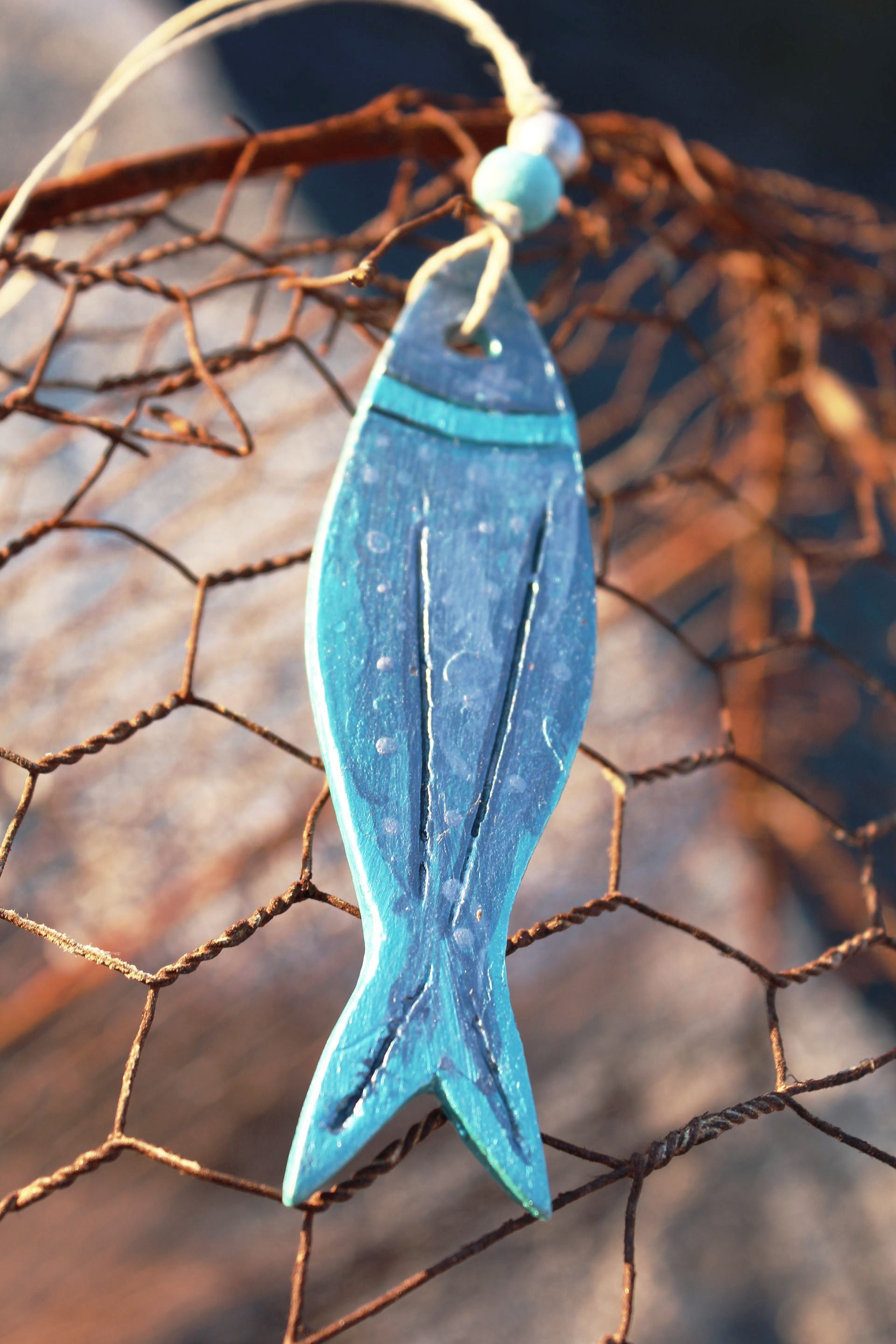 A blue fish ornament is hanging from a wire fence