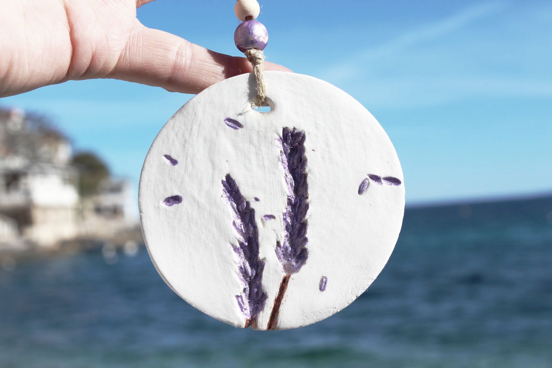 A person is holding a pendant with purple flowers on it in front of the ocean.