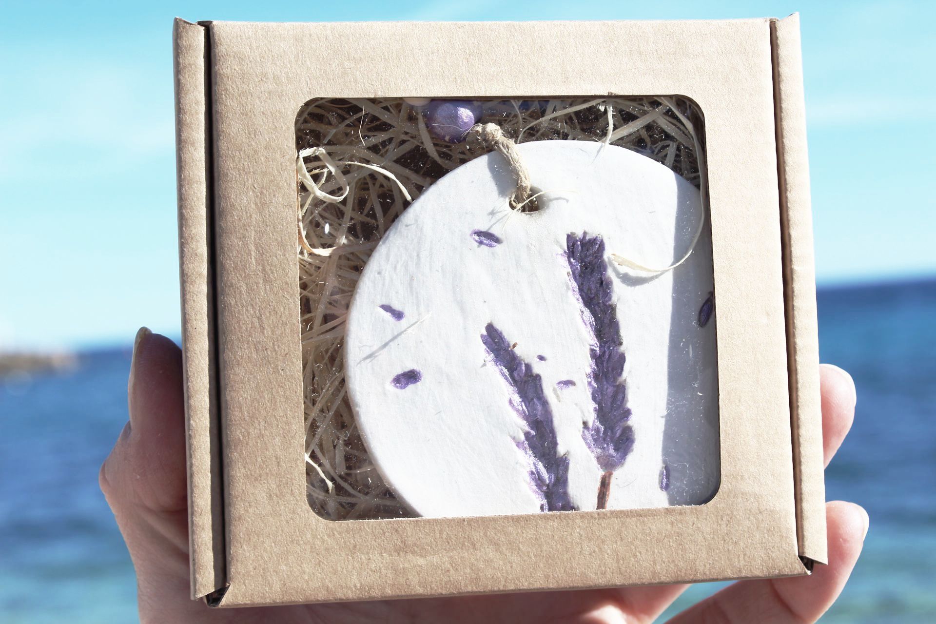A person is holding a cardboard box with a lavender ornament inside of it.