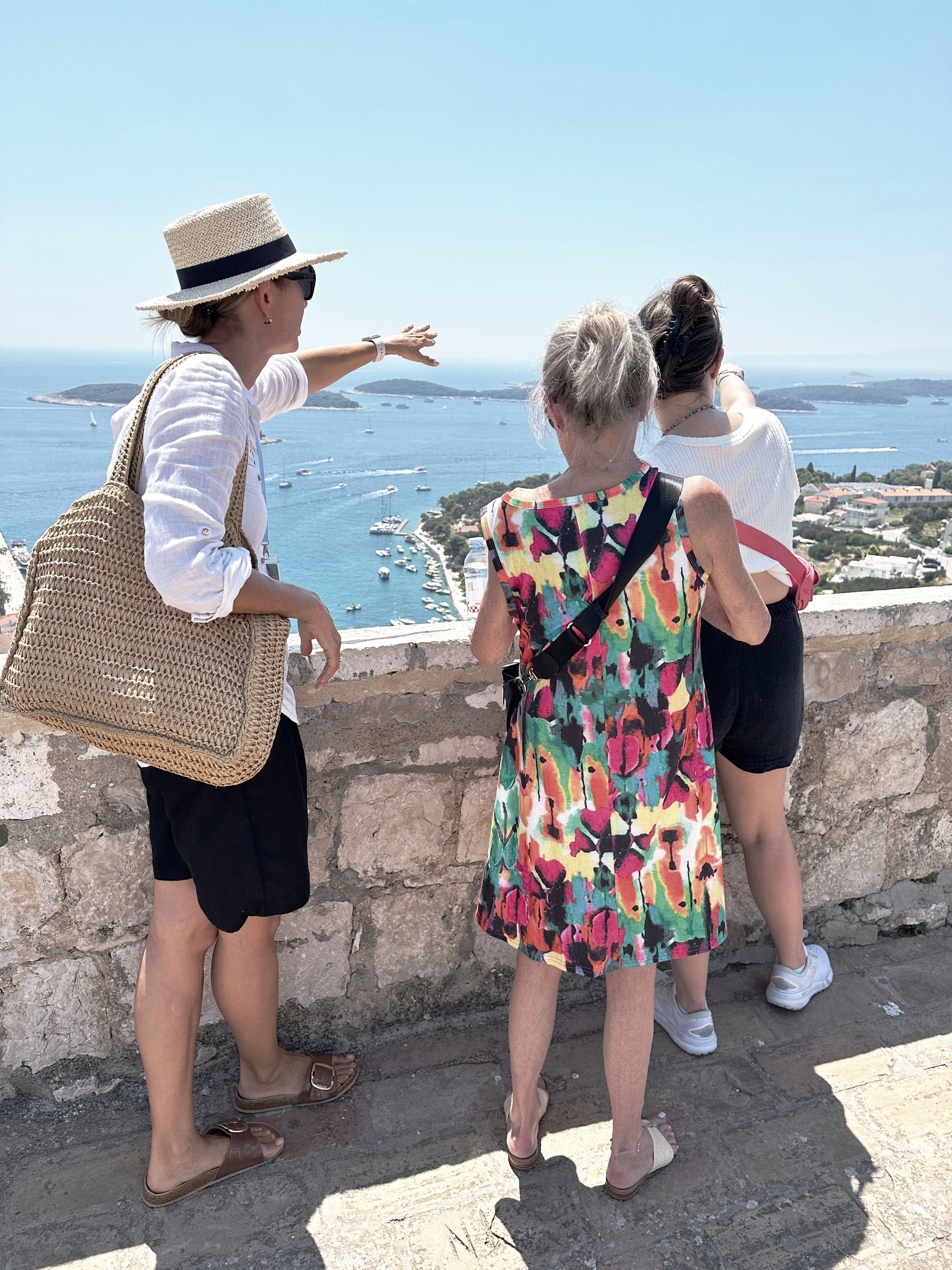 Three women are standing on a ledge overlooking the ocean.