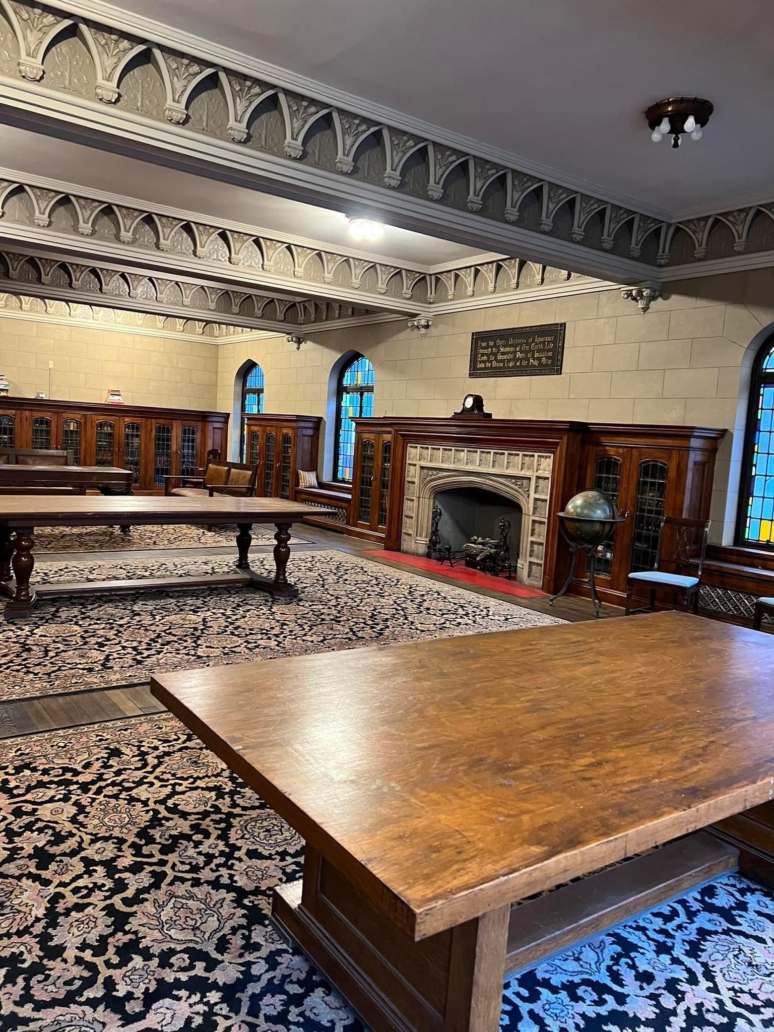 A large Library with tables, chairs, and a fireplace.