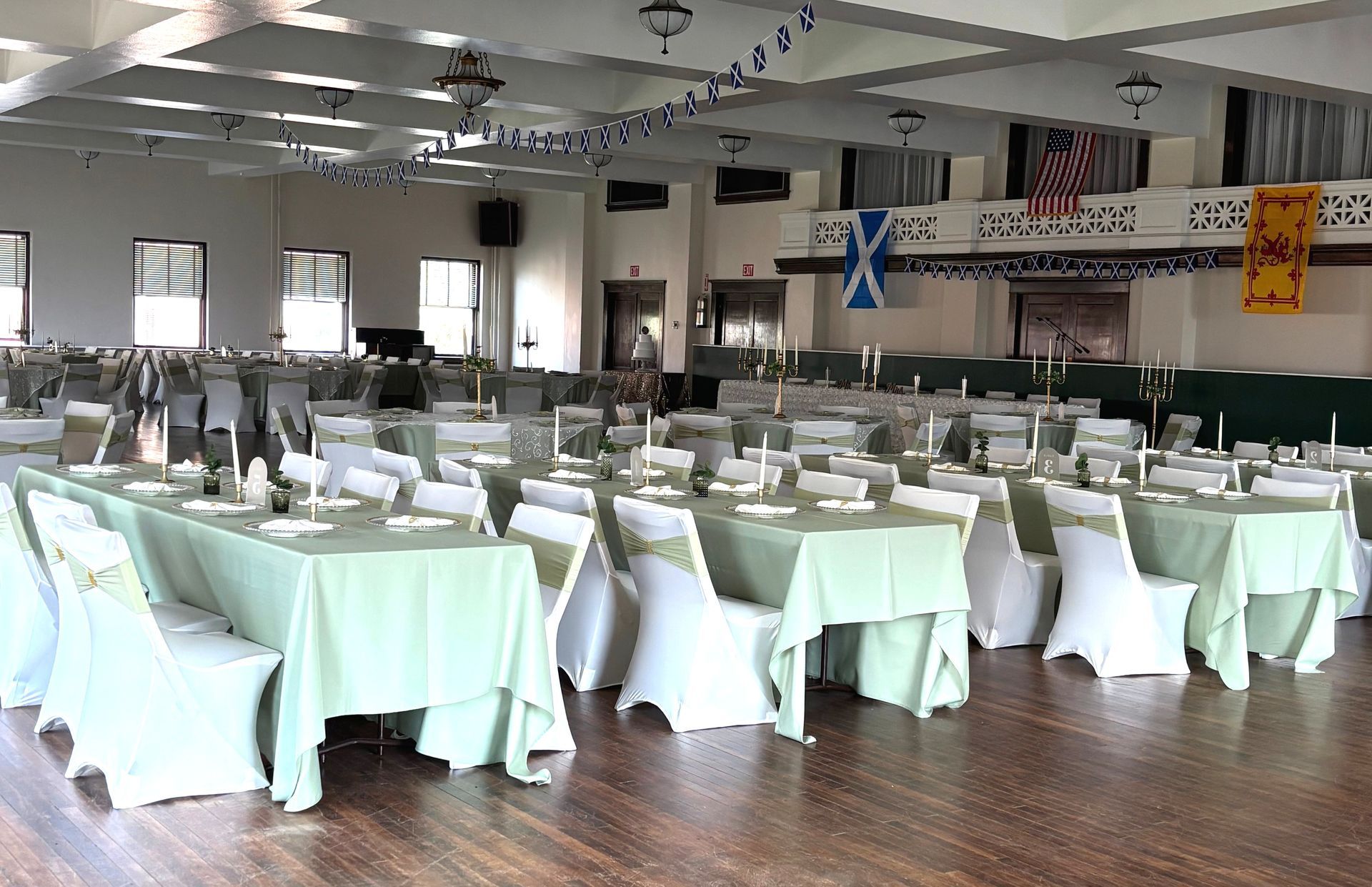 Large ballroom set for an event; tables covered in green, white chairs, Scottish flags, and American flag.