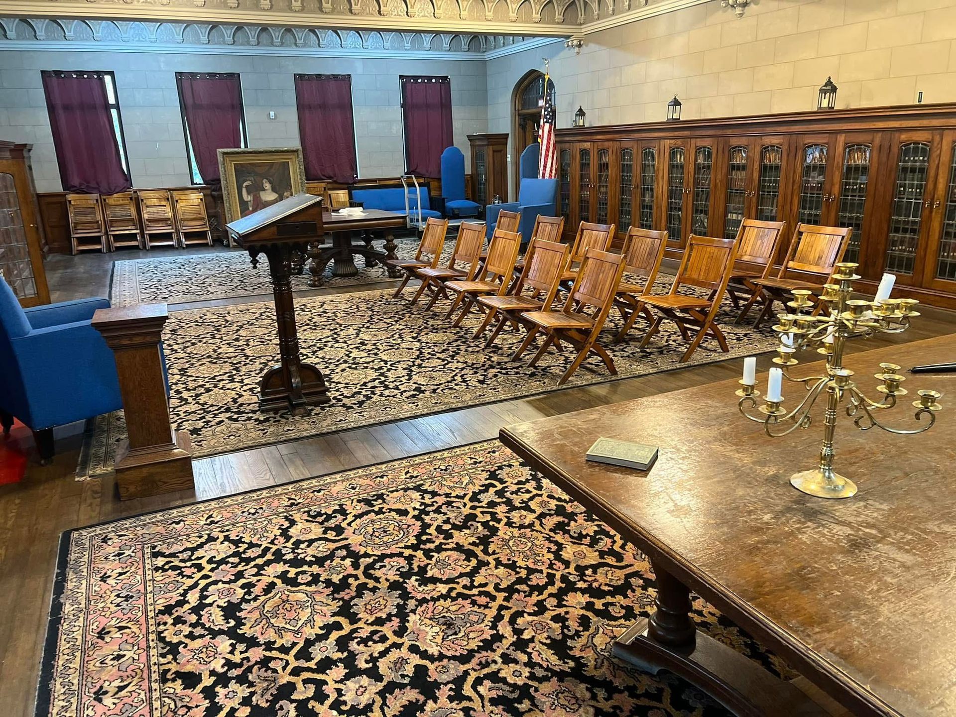 A large Library with a table, chairs, candles, and a rug.
