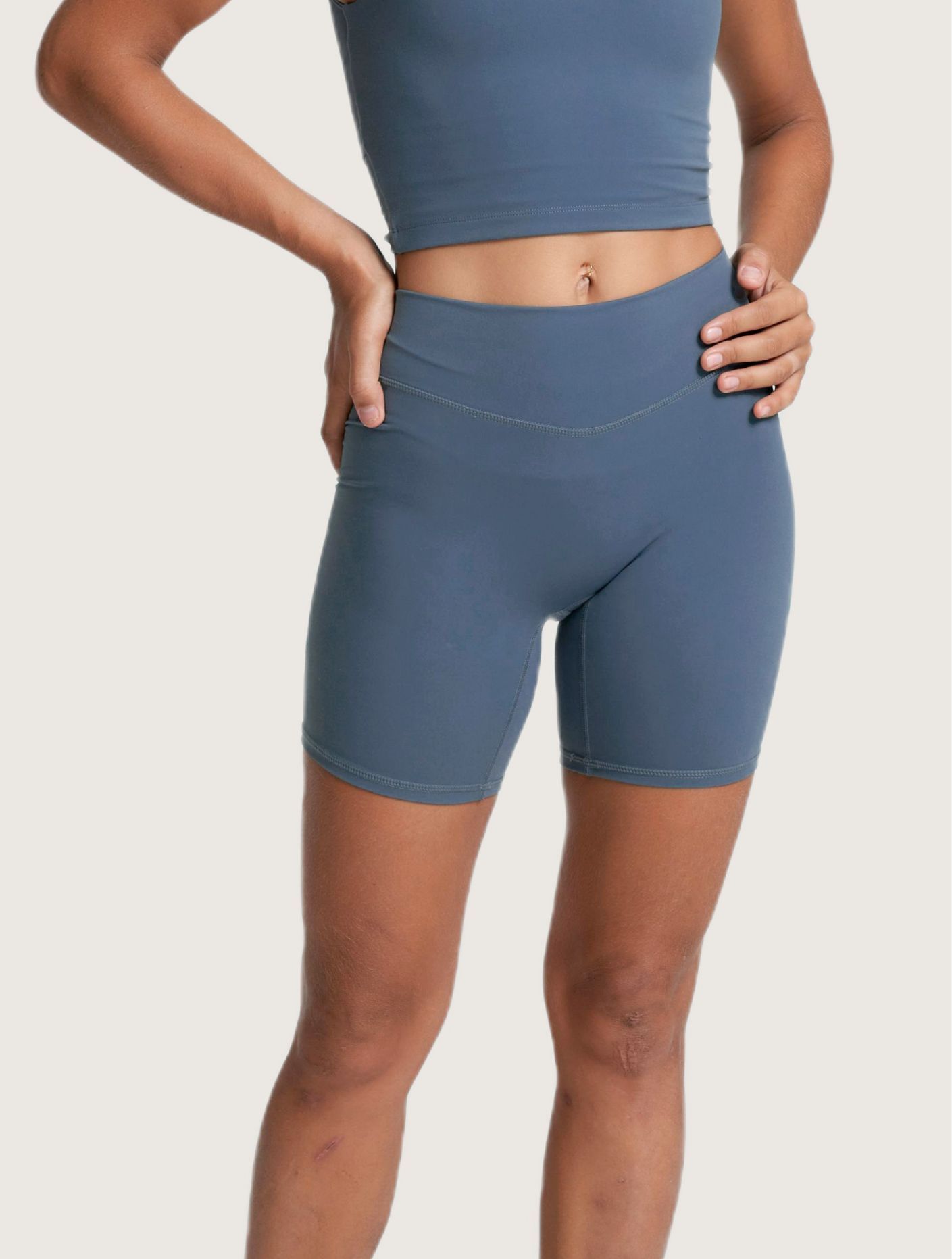 Woman in blue workout shorts and crop top, hands on hips.
