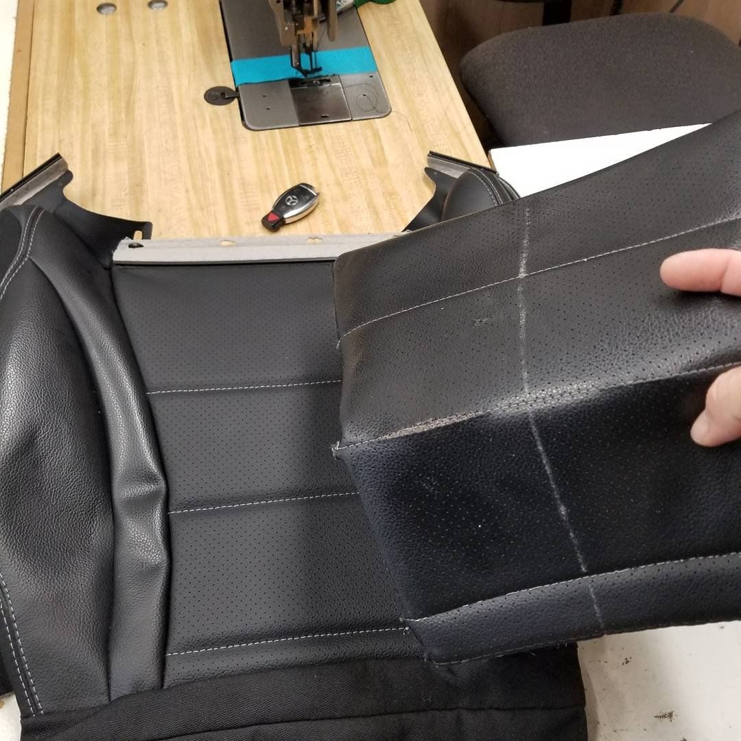 A person is holding a piece of black leather in front of a sewing machine