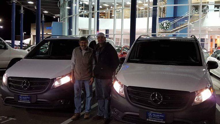 Two men are standing next to two mercedes vans in a parking lot.