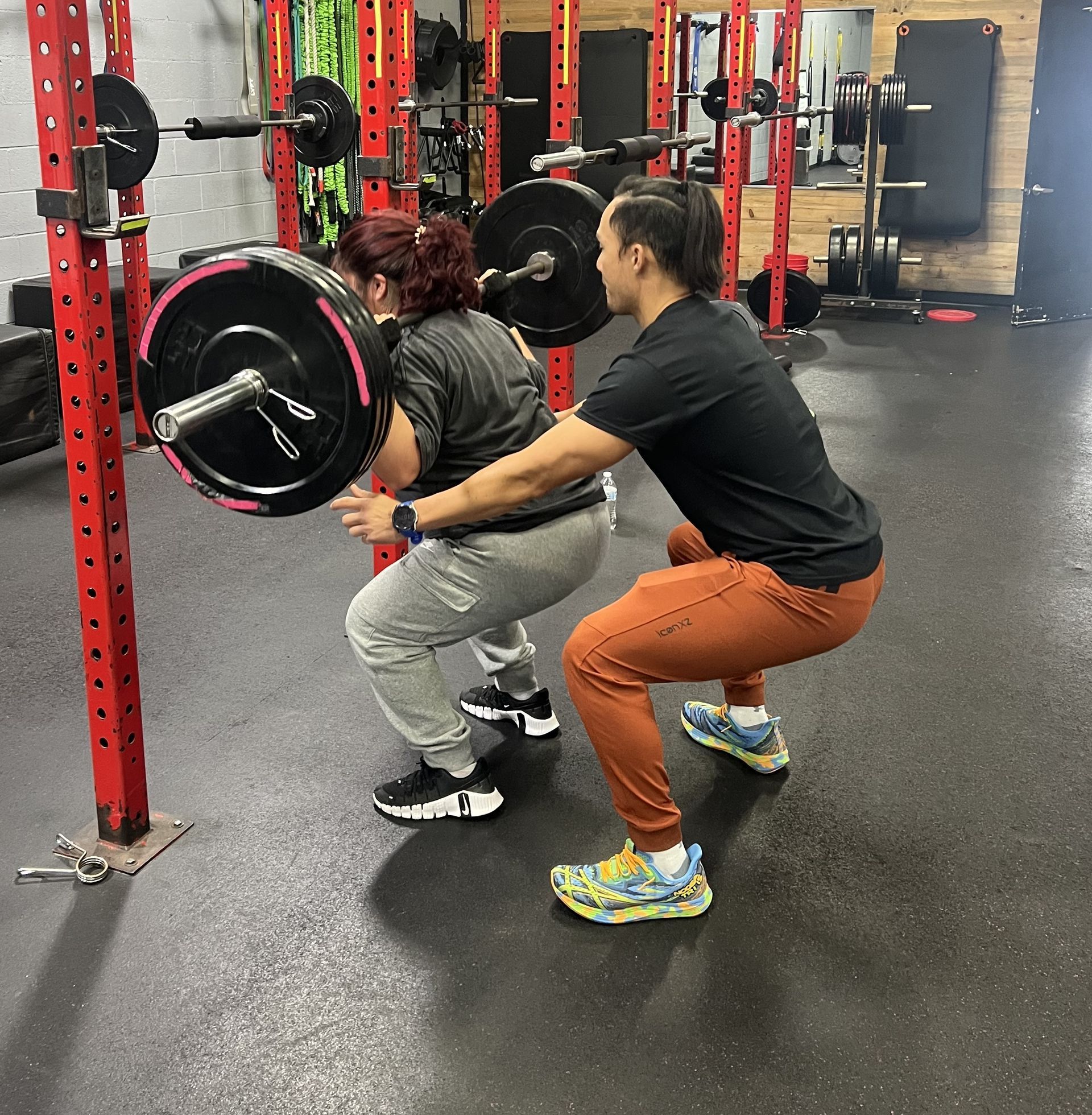 Man bench presses weight with a spotter at a gym. Red and black weights and equipment.