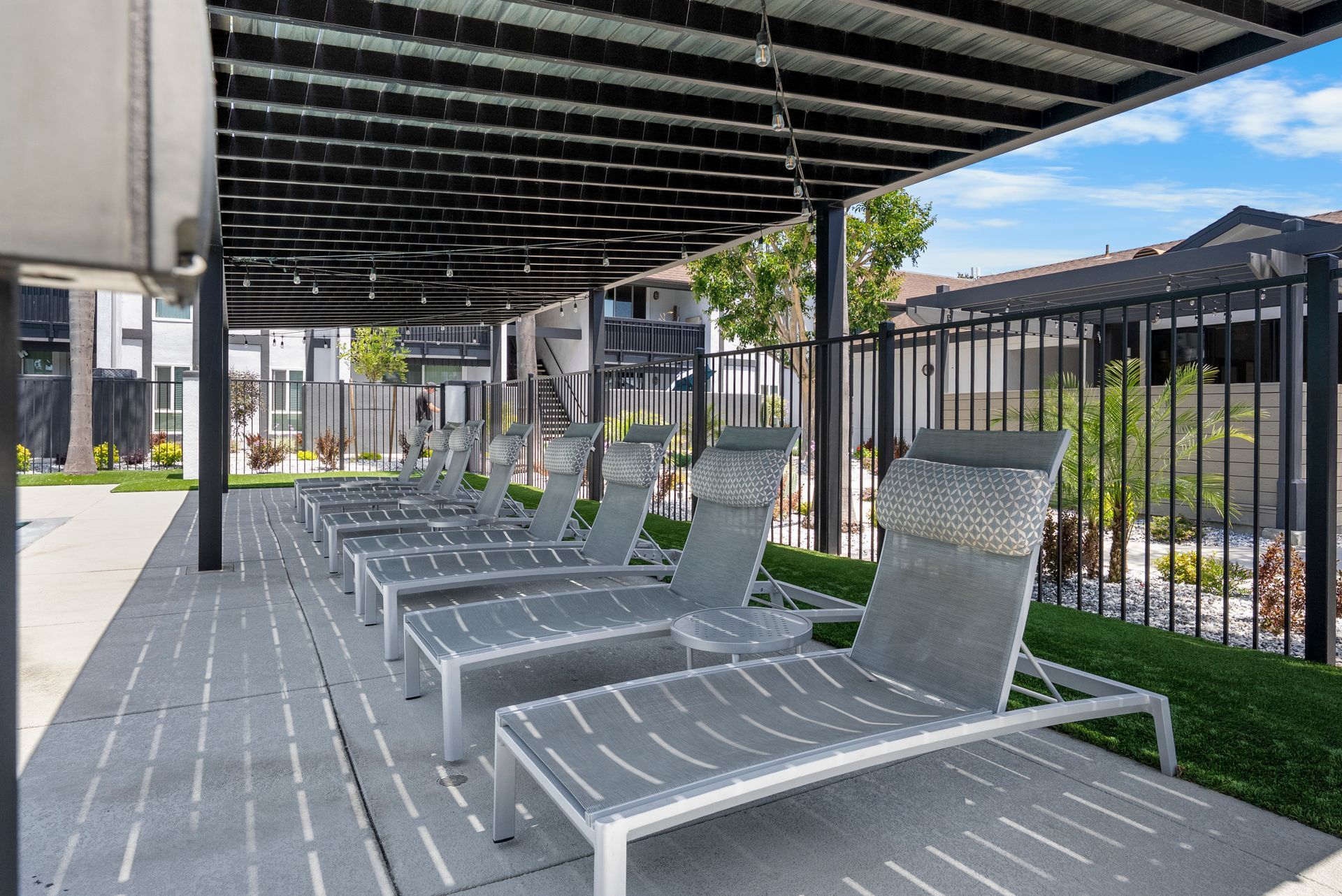 A row of lounge chairs under a canopy next to a pool.