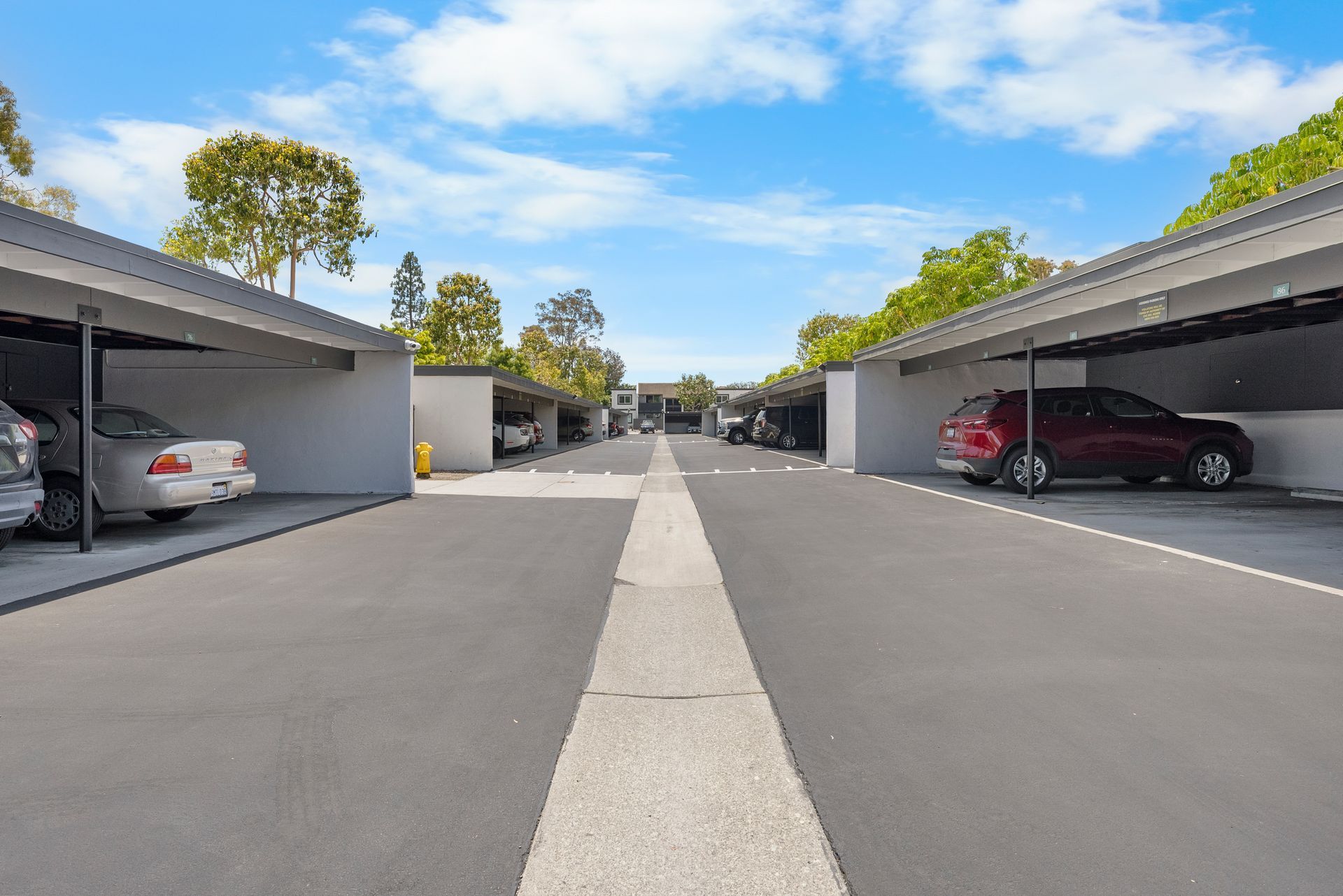 A row of cars are parked in a covered parking lot.